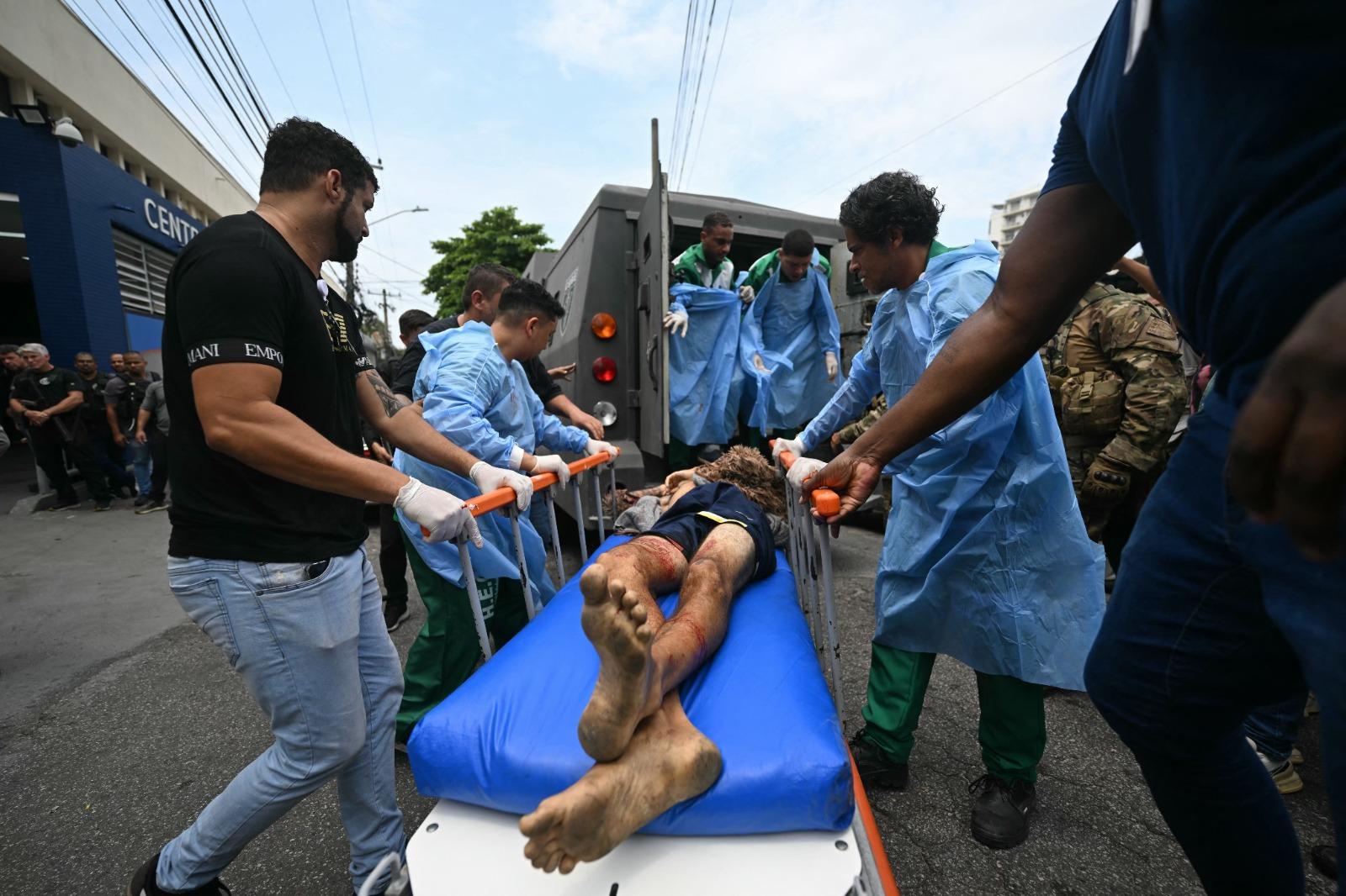 Homem ferido é levado de maca para dentro de veículo blindado.