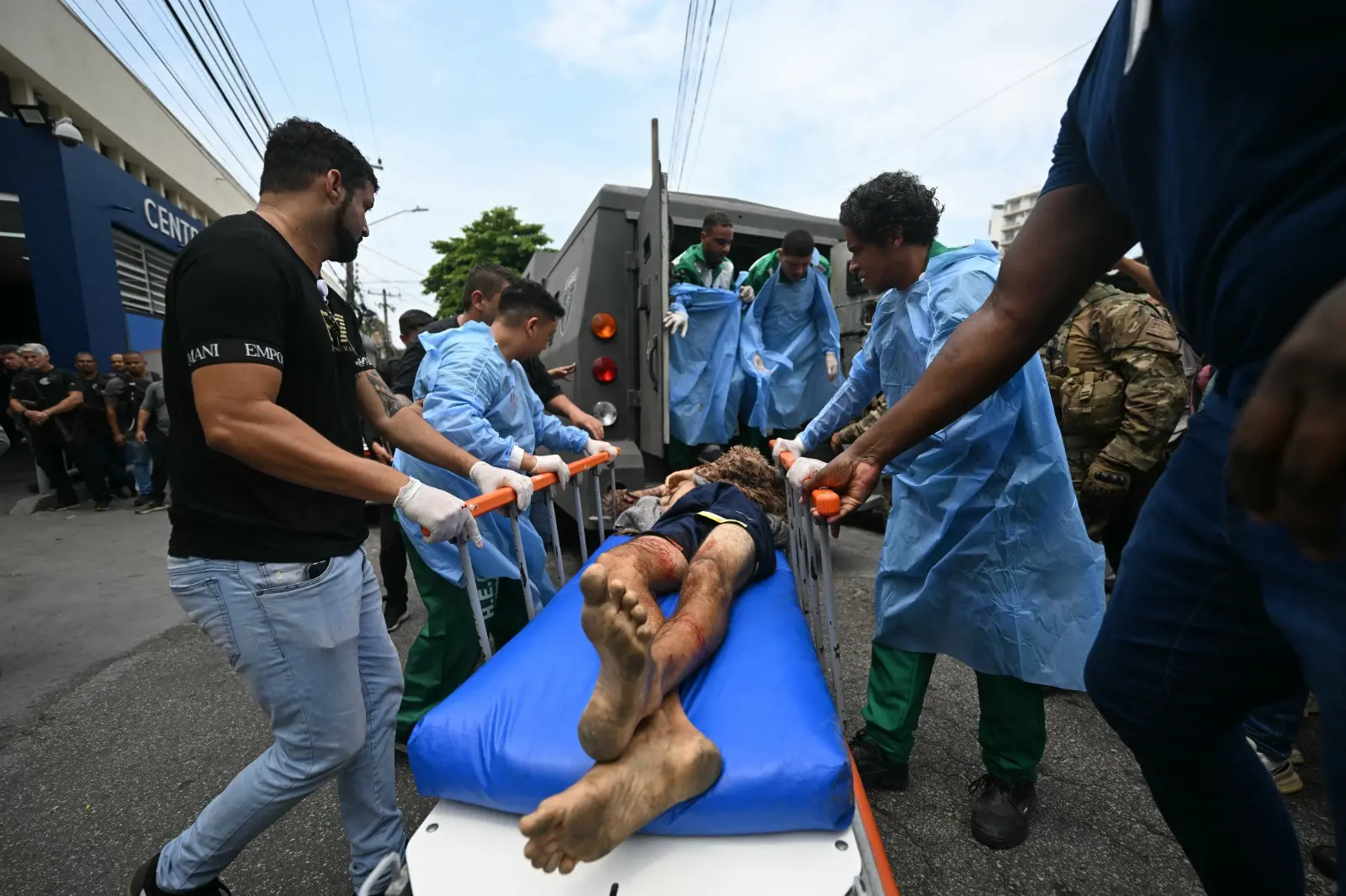Homem ferido é levado de maca para dentro de veículo blindado.