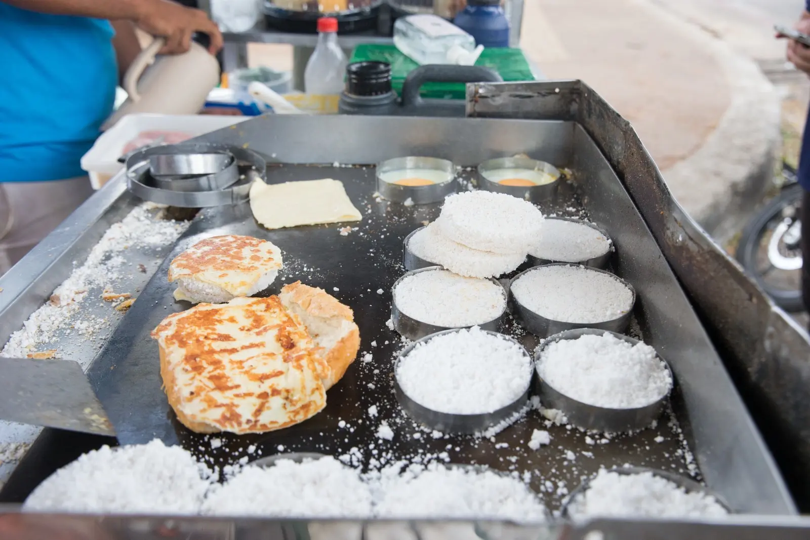 Pão na chapa com queijo derretido e, à direita, tapiocas redondas na chapa, em formas também redondas.