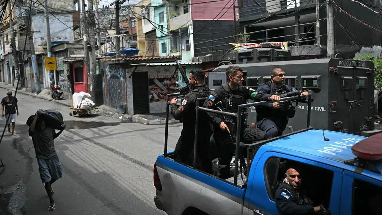 A foto mostra uma operação policial em uma área urbana com agentes armados em um veículo pick-up e um blindado ao fundo. Imagem usada em matéria onde Lula classifica megaoperação do Rio como matança.