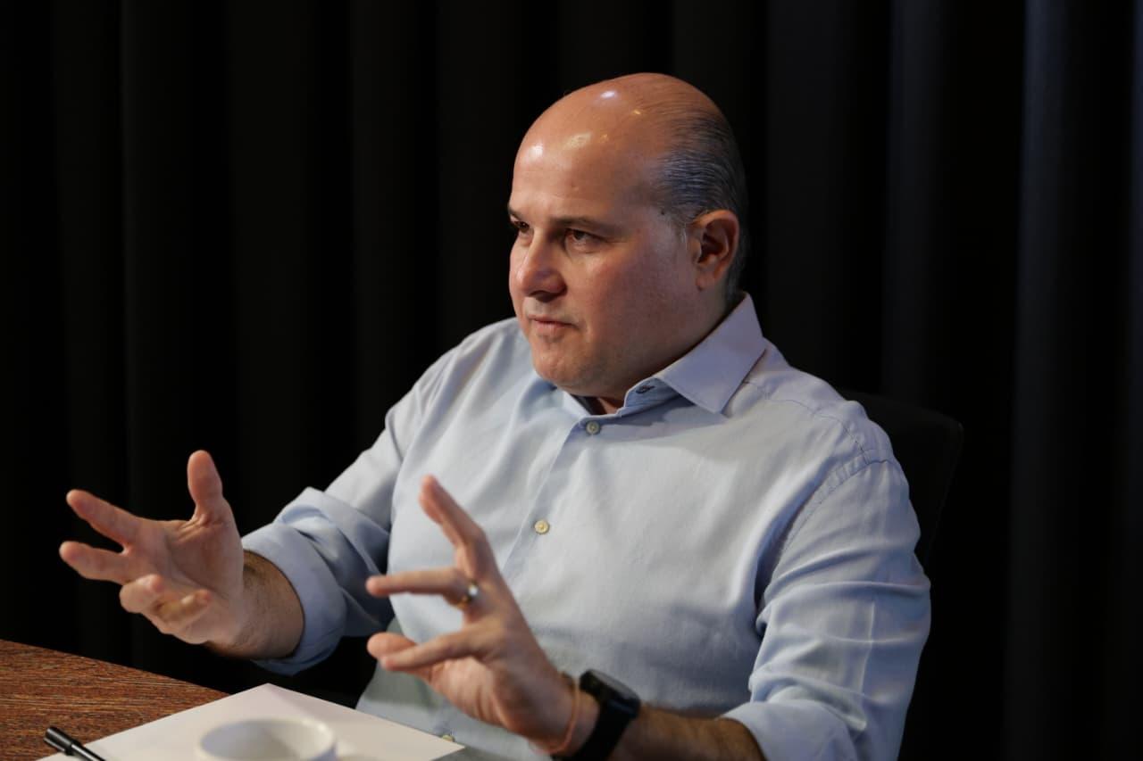 Roberto Cláudio gesticula enquanto concede entrevista. Ele veste uma camisa azul e está sentado