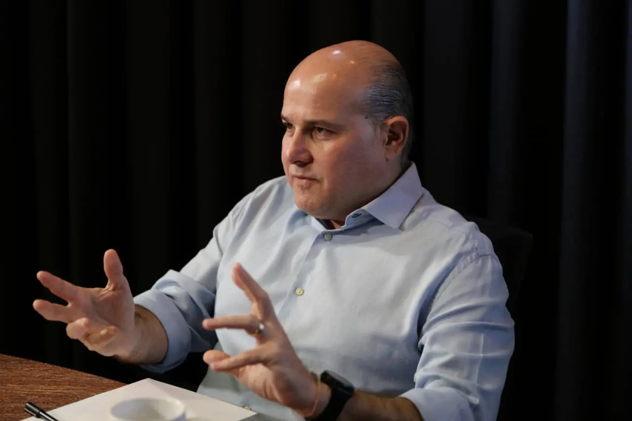 Roberto Cláudio gesticula enquanto concede entrevista. Ele veste uma camisa azul e está sentado