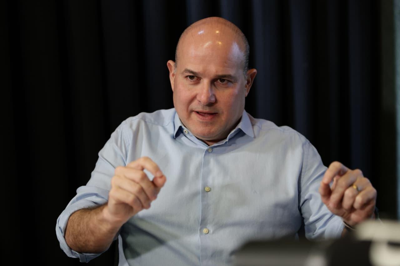 O ex-prefeito de Fortaleza, Roberto Cláudio, gesticula enquanto fala durante entrevista. Ele veste camisa azul clara e aparece em ambiente interno, com fundo escuro.