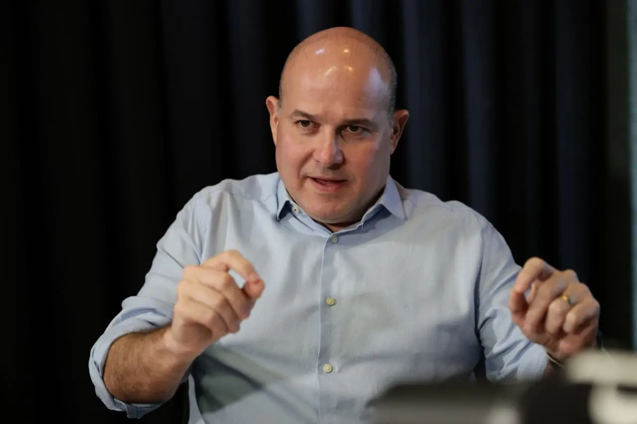 O ex-prefeito de Fortaleza, Roberto Cláudio, gesticula enquanto fala durante entrevista. Ele veste camisa azul clara e aparece em ambiente interno, com fundo escuro.
