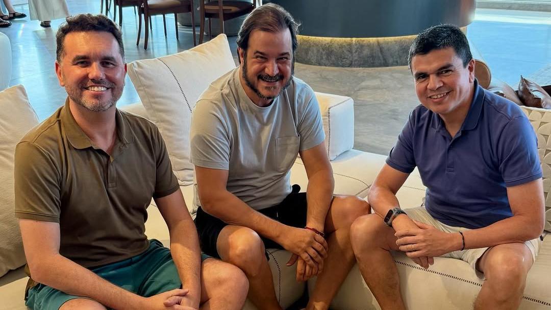 Moses e Rueda durante encontro com Chagas Vieira, secretário da Casa Civil. Os três estão sentados, com camisetas e bermudas. Os três estão sorrindo para a foto.