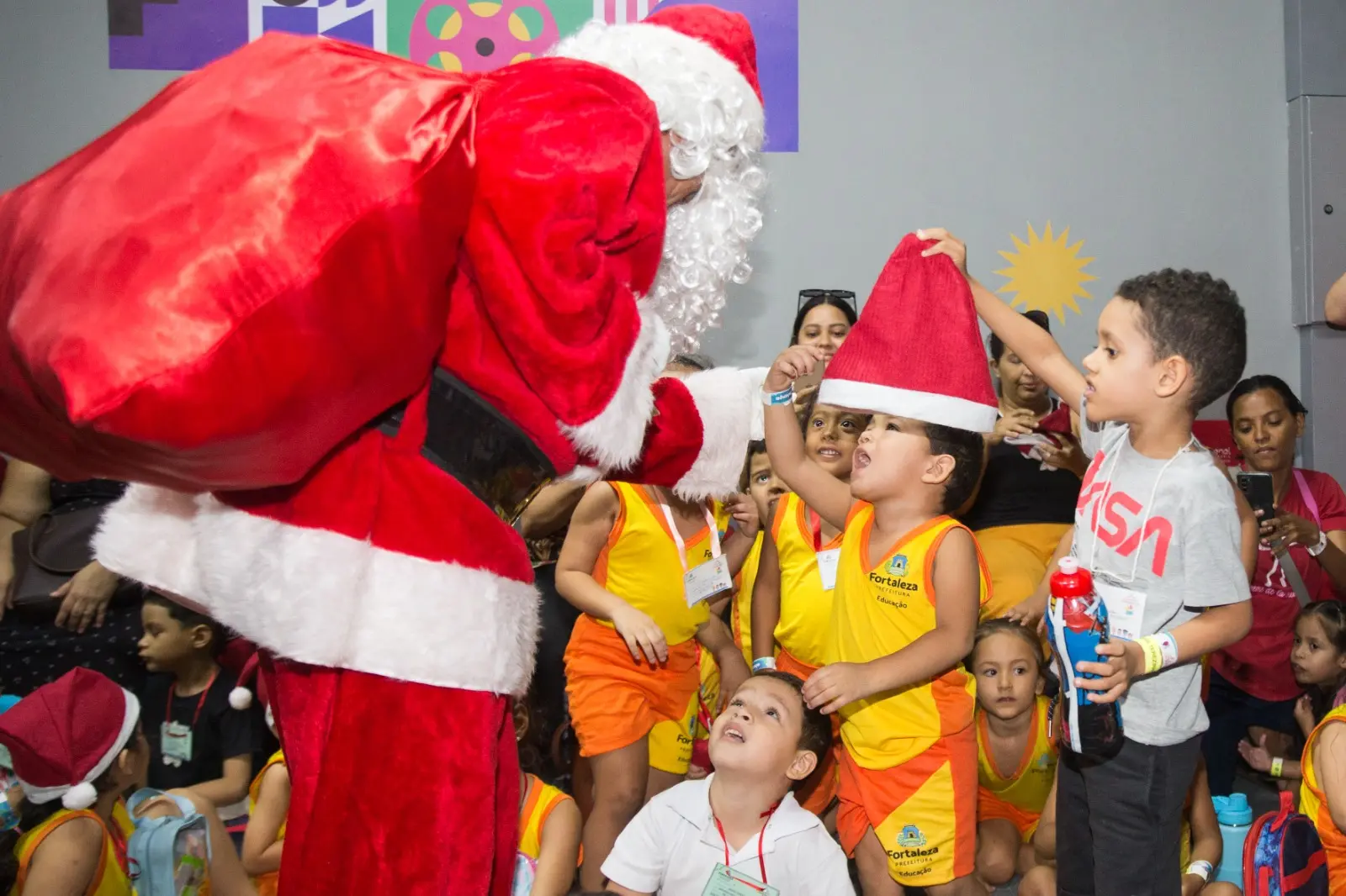 Na imagem, um homem vestido de Papai Noel entrega presente a crianças em Fortaleza.
