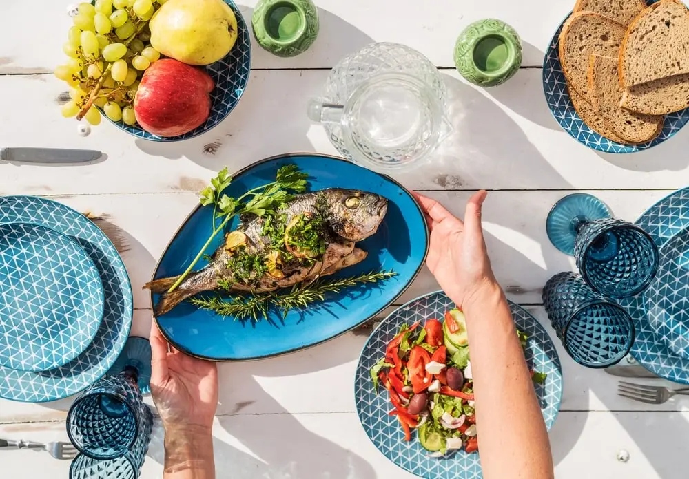 foto de mesa posta com peixe, salada e frutas. Imagem para ilustrar matéria sobre alimentos que ajudam a espantar o mau humor.