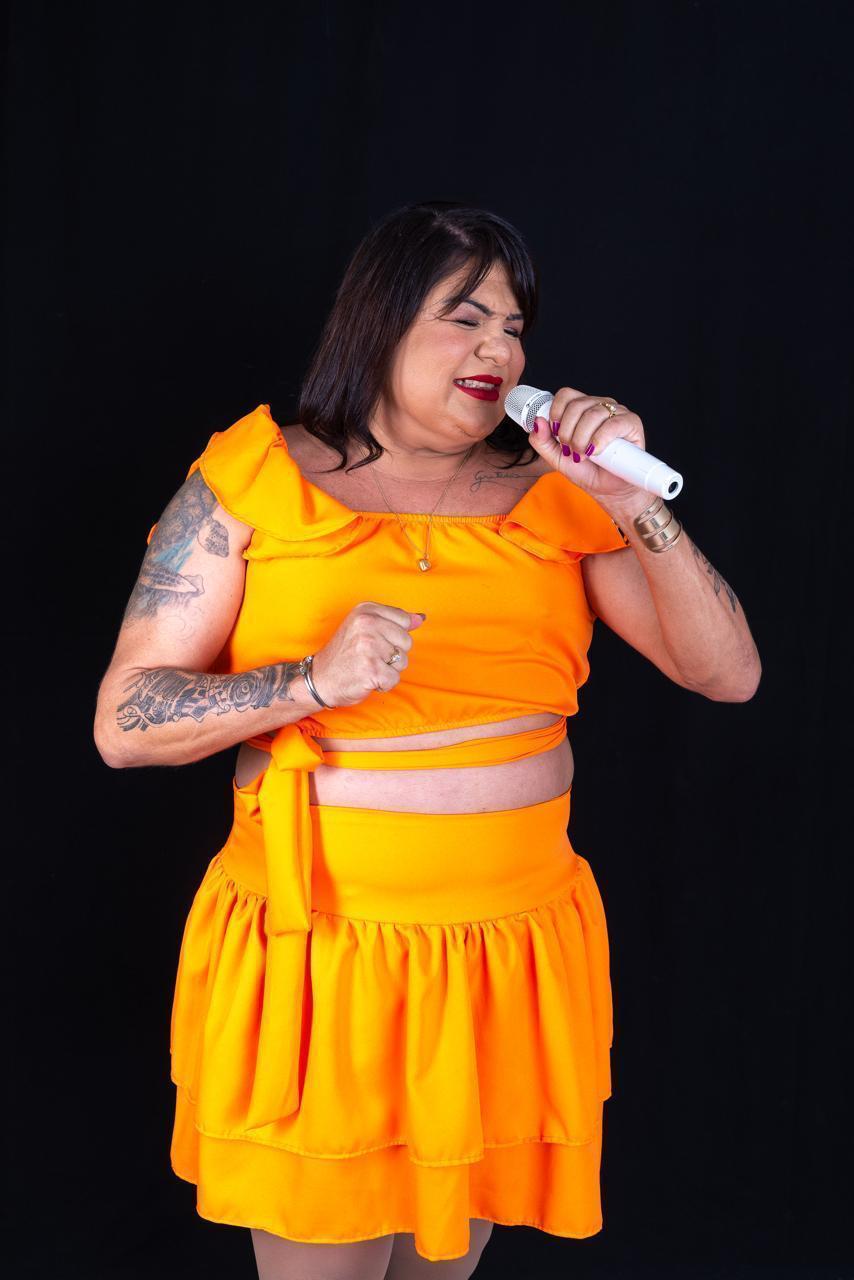 Cantora Zeza dos Teclados, cantando segurando um microfone vestida em um conjunto laranja.