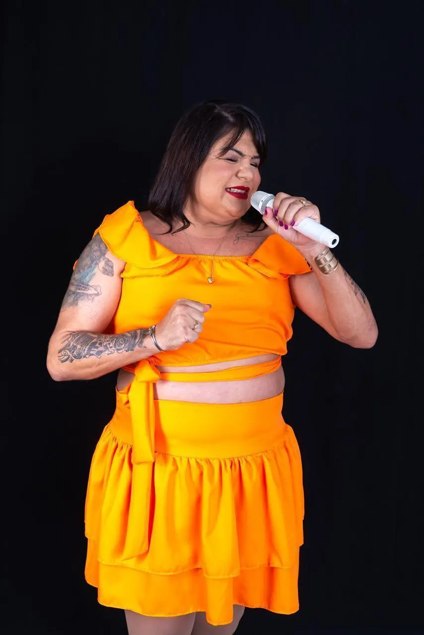 Cantora Zeza dos Teclados, cantando segurando um microfone vestida em um conjunto laranja.