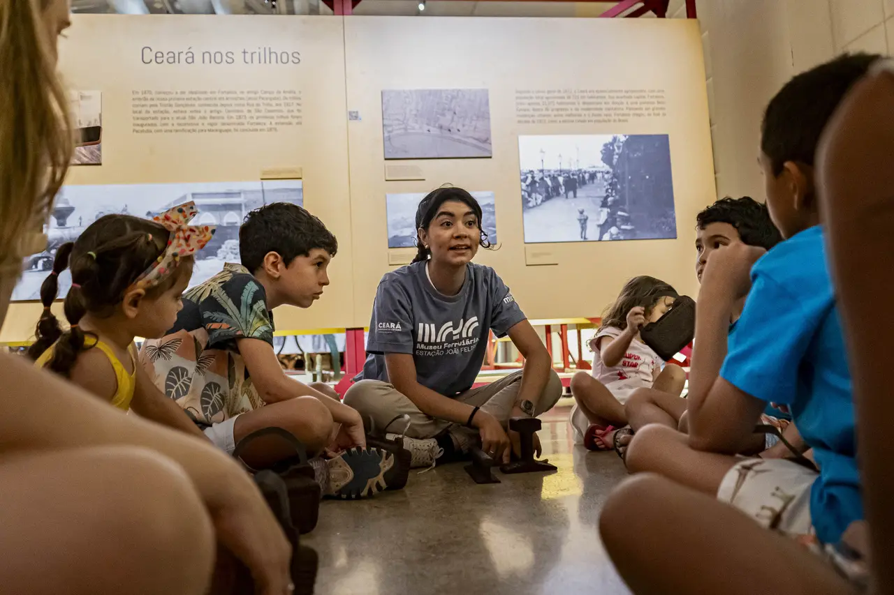 Uma arte-educadora sentada no chão, em frente a um painel com o título 