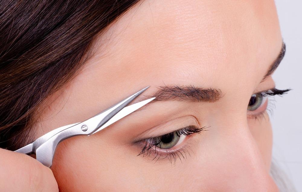 foto de mulher aparando os pelos da sobrancelha com uma tesoura.