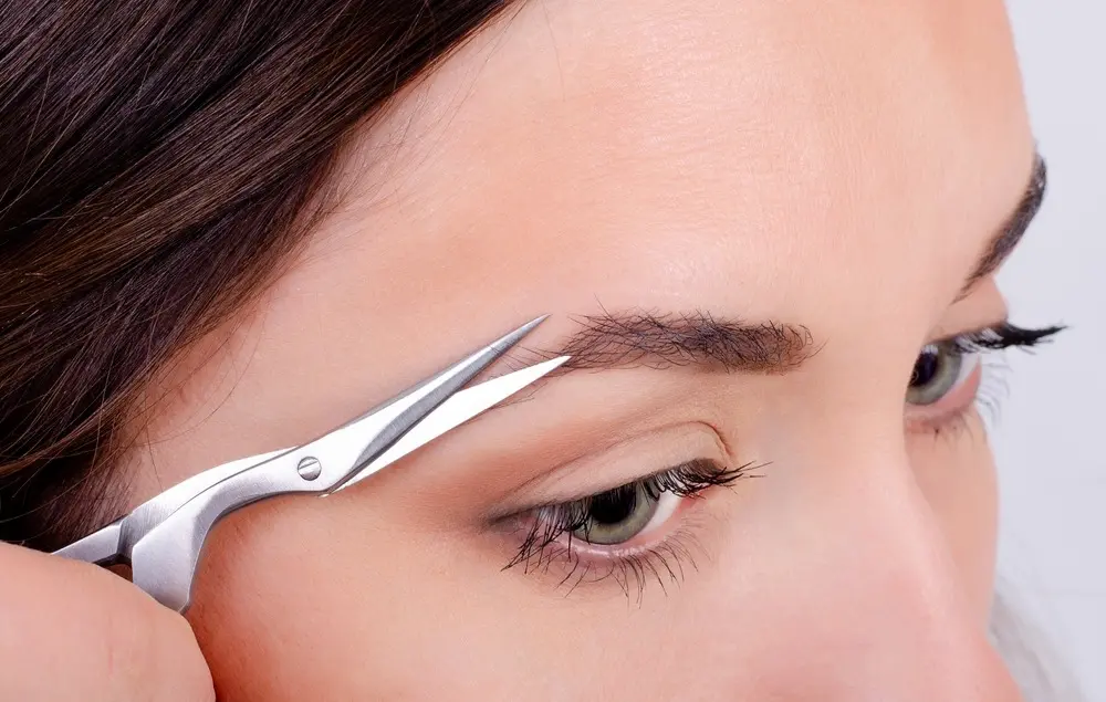 foto de mulher aparando os pelos da sobrancelha com uma tesoura.