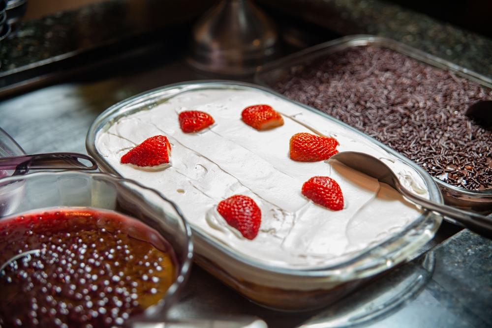 Pavê com decorações de morango e chocolate ao lado de sobremesas.