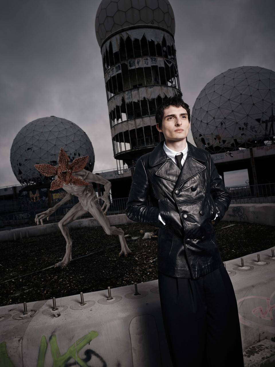 Foto de ativação de Finn Wolfhard em Stranger Things vestindo casaco de couro preto e olhando para o lado.