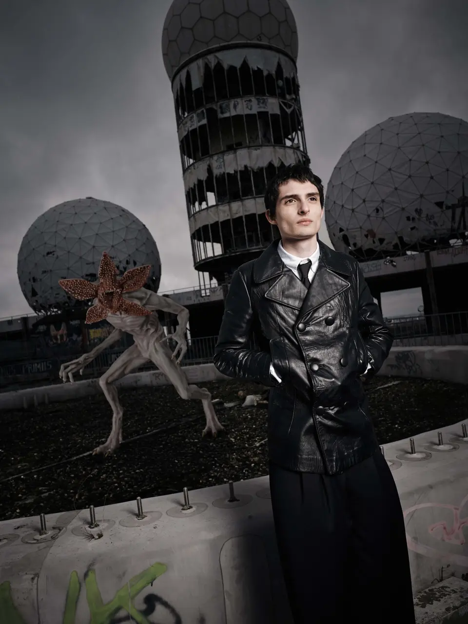 Foto de ativação de Finn Wolfhard em Stranger Things vestindo casaco de couro preto e olhando para o lado.