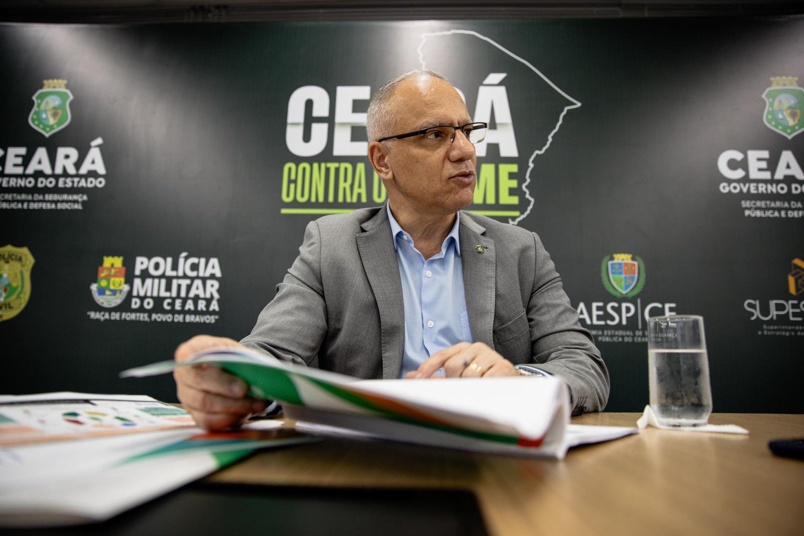 A foto mostra o secretário da Segurança Pública do Ceará, Roberto Sá, um homem de cor parda, óculos e cabelo branco, que veste um terno e blusa social. Ele está com um papel na mão.