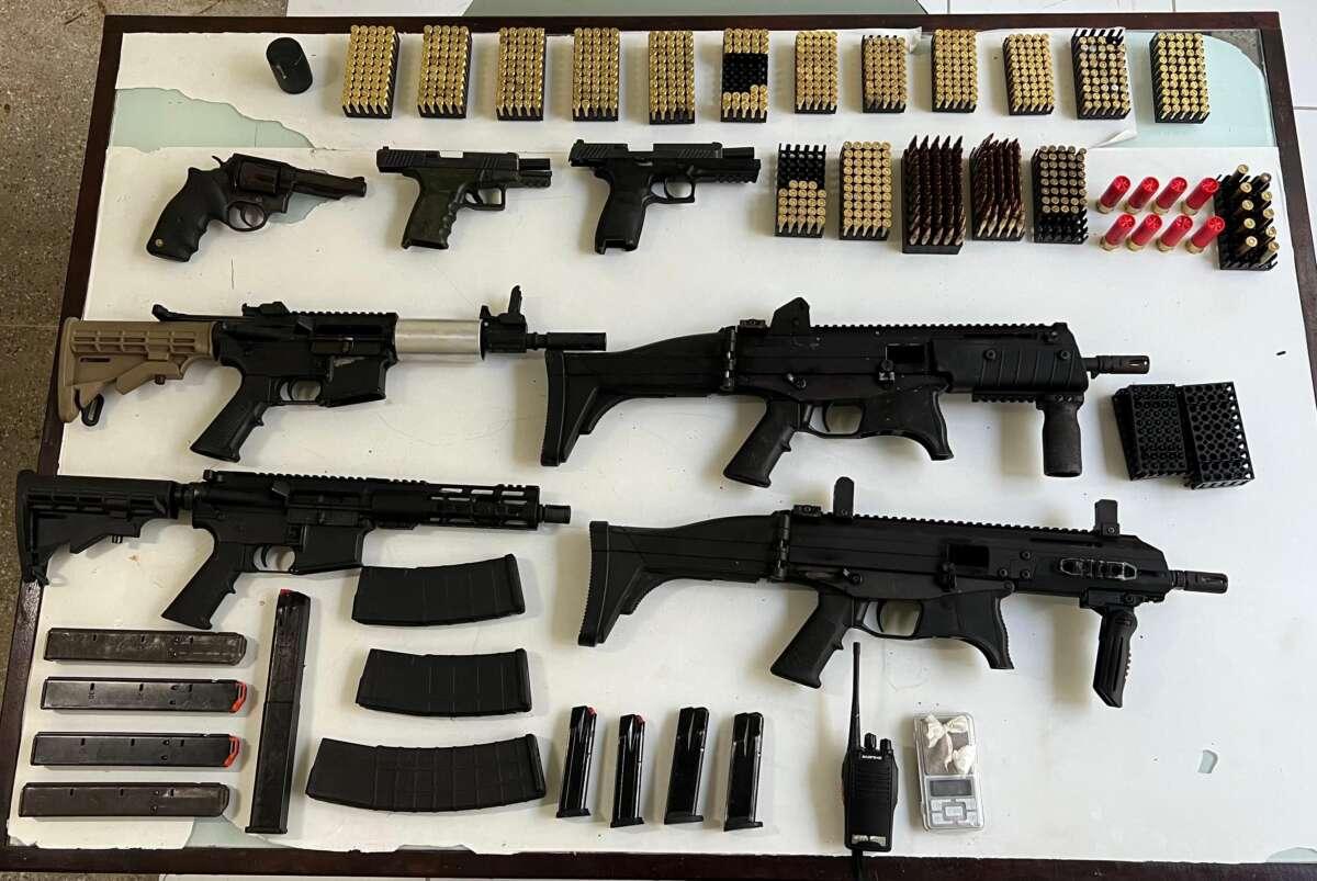 A foto mostra várias armas de fogo e munições, apreendidas pela Polícia, em cima de uma mesa branca.