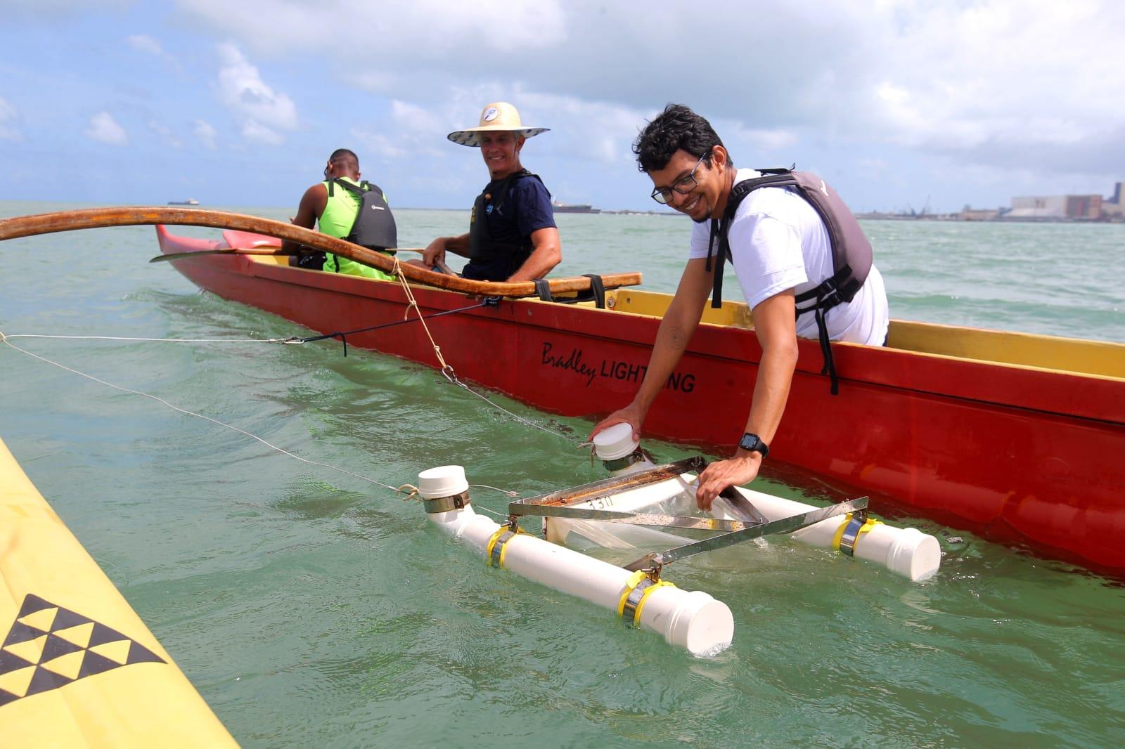 Pesquisadores realizando coleta de dados na água usando equipamento de monitoramento em uma embarcação no oceano, com céu parcialmente nublado ao fundo.