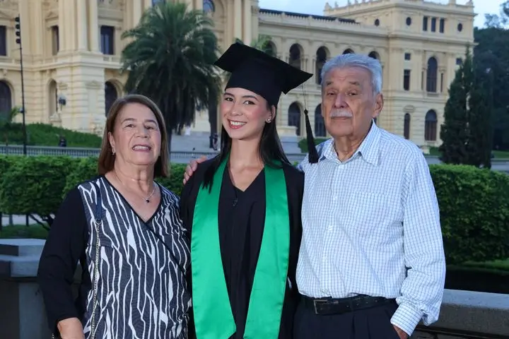 Na imagem a jovem está posando para a foto de formatura com seus avós.
