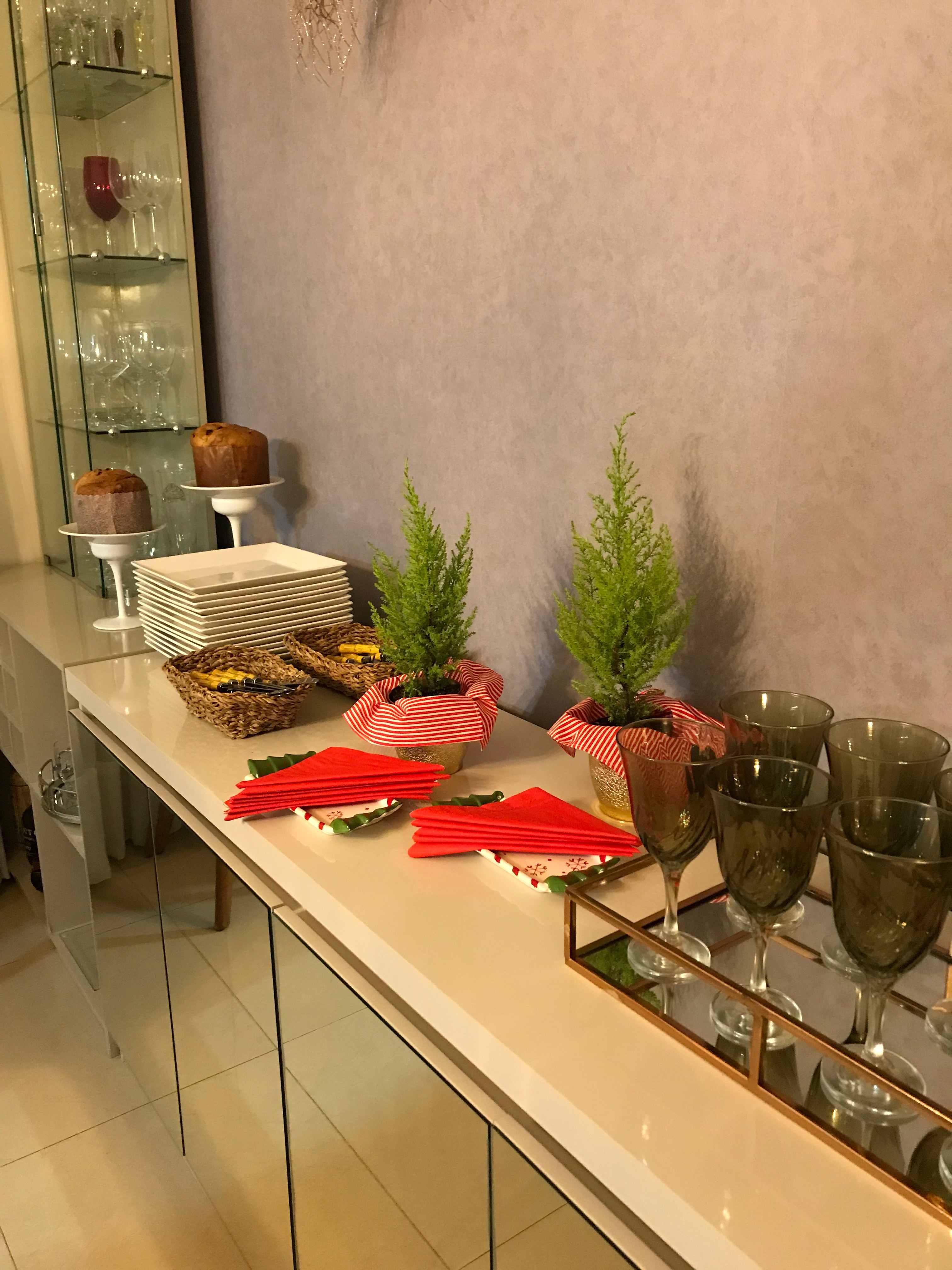 Esta cena exibe um elegante balcão de buffet preparado para uma confraternização, onde a organização se une à festividade natalina através de detalhes temáticos. No centro da composição, destacam-se dois pequenos 