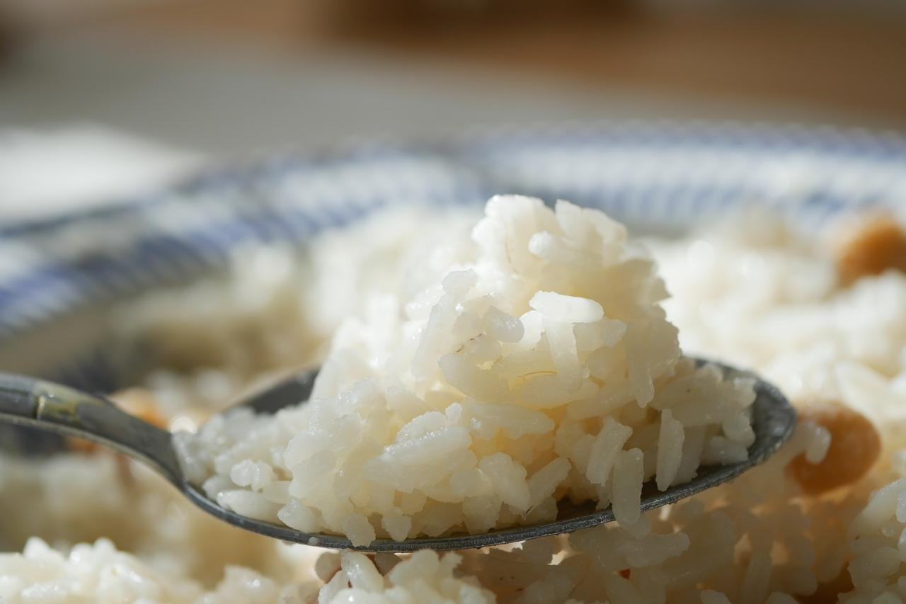Colher de arroz branco em foco, com prato azulado cheio de arroz em segundo plano.