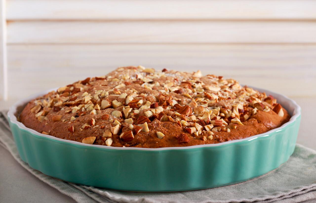 Travessa redonda verde com bolo baixo dentro, recheado com nozes na parte superior.