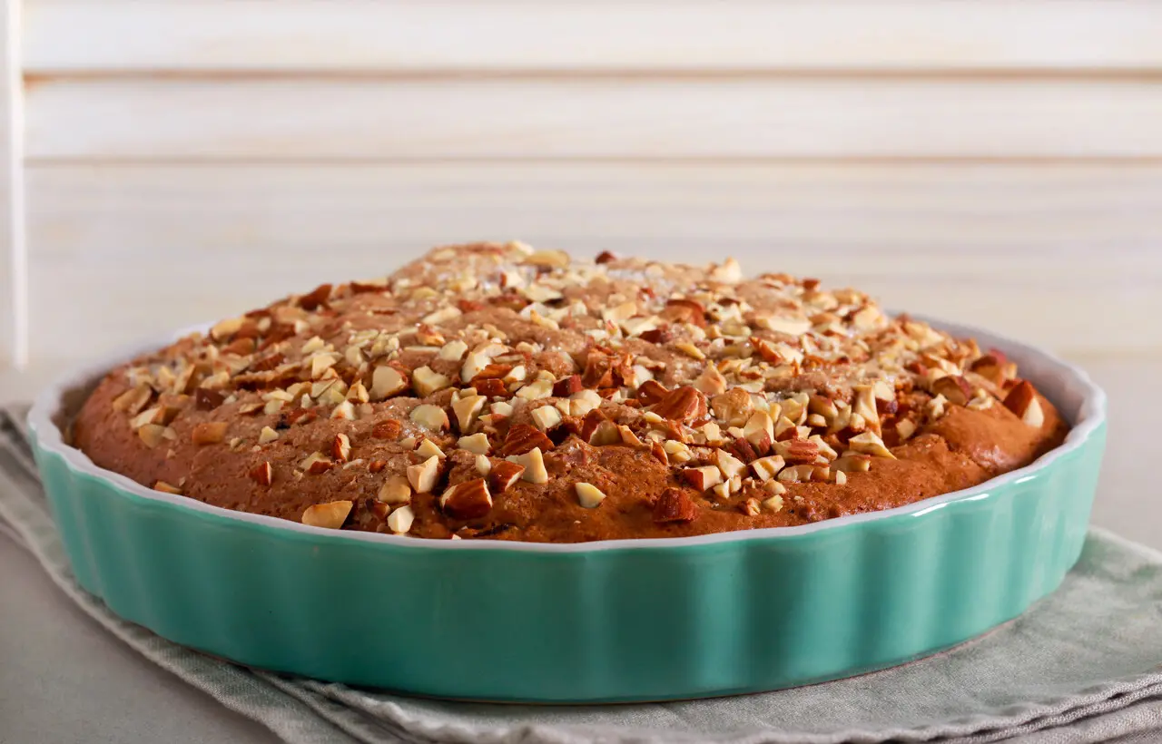 Travessa redonda verde com bolo baixo dentro, recheado com nozes na parte superior.