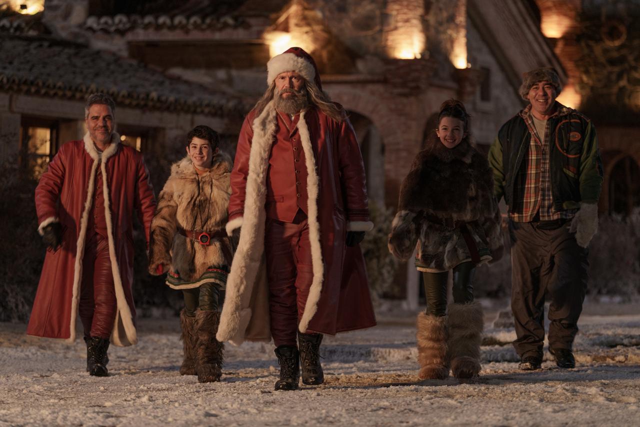 Cinco pessoas andando em chão coberto por neve, vestindo casacos grandes e vermelhos.