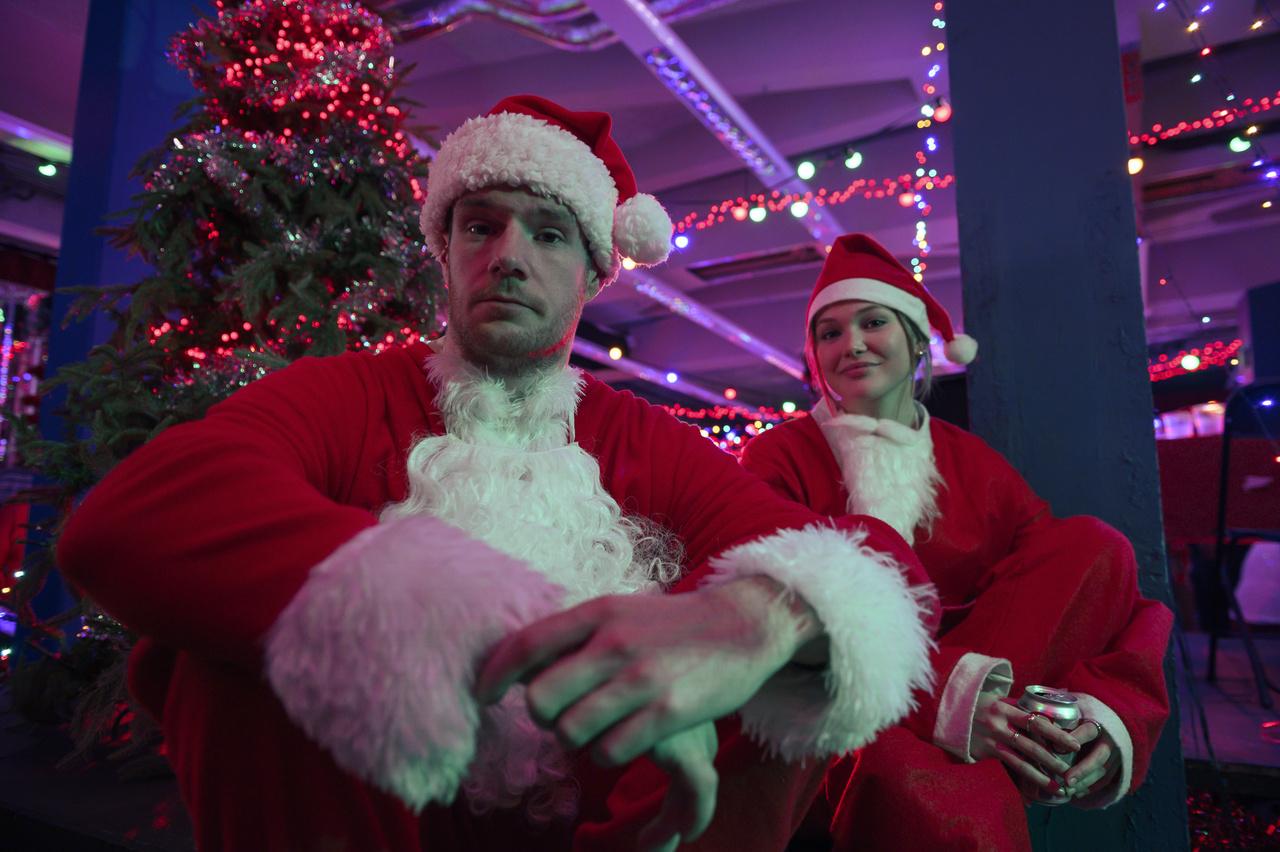Duas pessoas em roupas parecidas com as do Papai Noel, com gorro vermelho na cabeça.
