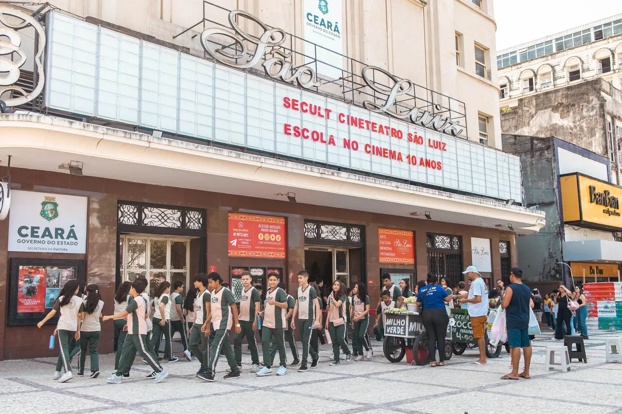 Uma foto tirada em ângulo aberto e ligeiramente de baixo para cima mostra a fachada do icônico Cineteatro São Luiz em Fortaleza, Ceará, com um grupo de estudantes uniformizados entrando no cinema.