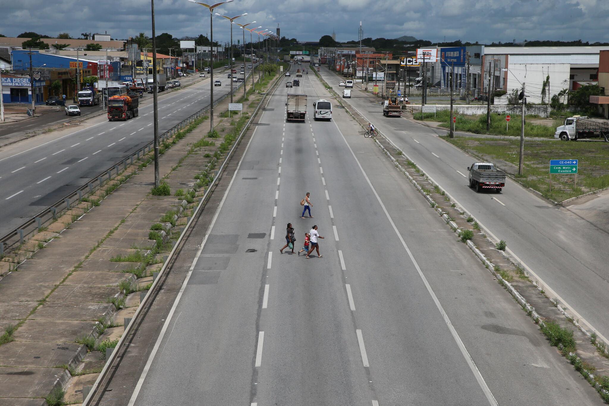 Foto ampla da pista da BR-116 com três pessoas atravessando a via.