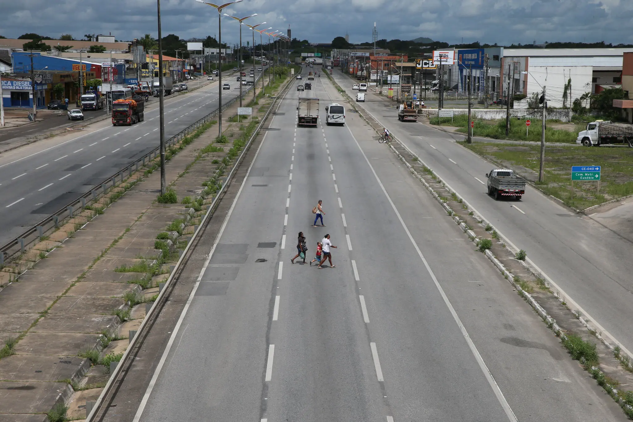 Foto ampla da pista da BR-116 com três pessoas atravessando a via.