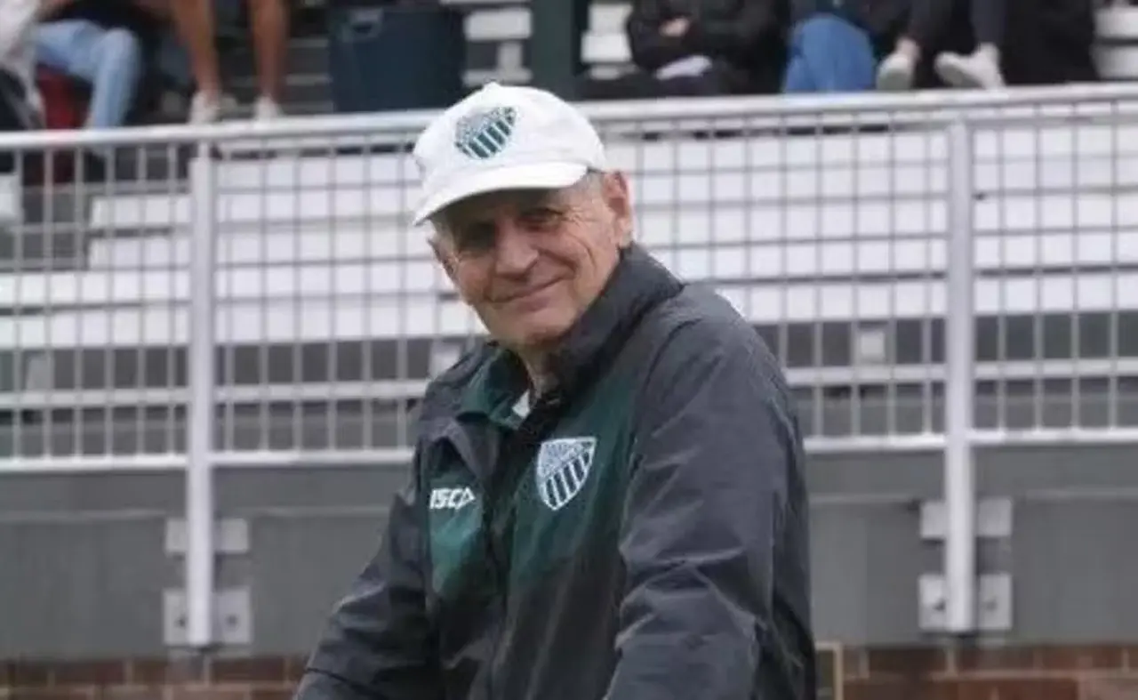 Homem branco de boné branco com escudo de time preto e branco e jaqueta preta com mesmo símbolo.