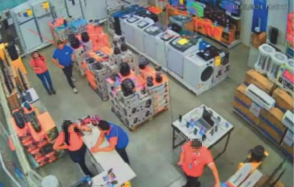 A imagem de uma câmera de segurança mostra a movimentação de um supermercado, no setor de eletrodomésticos, com cinco pessoas e dezenas de produtos.
