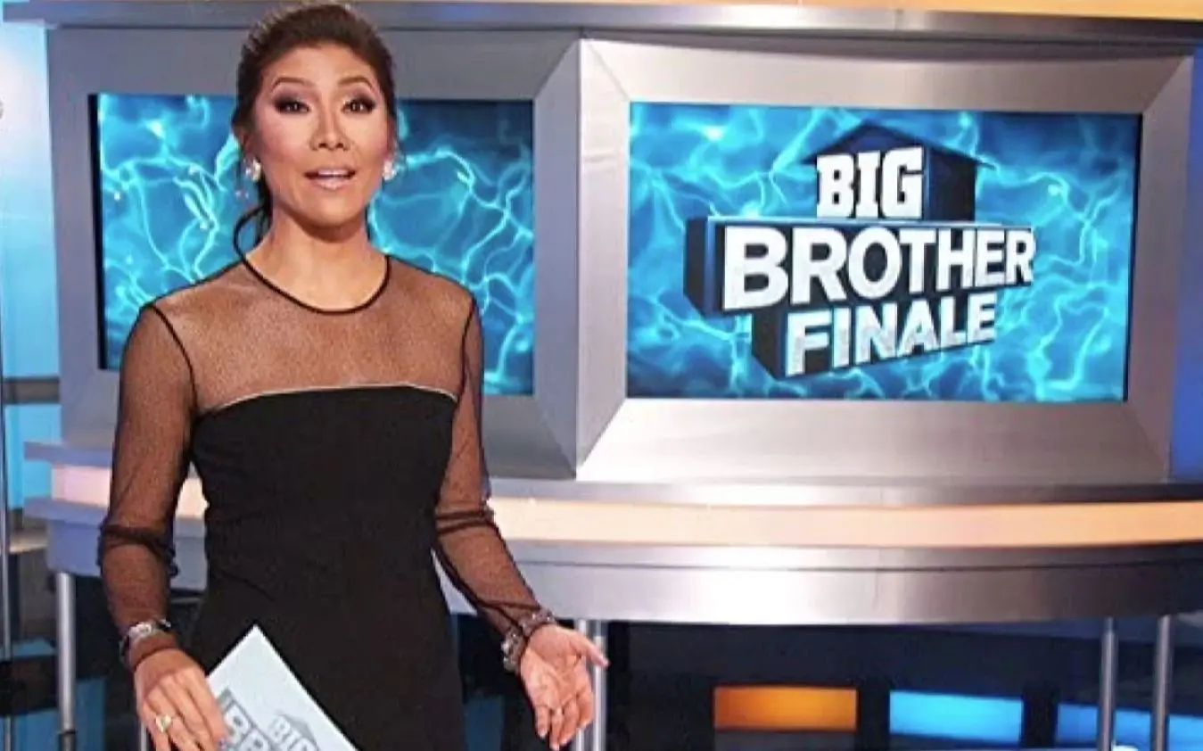 Apresentador em estúdio diante de telas com o texto 'BIG BROTHER FINALE' sobre fundo azul elétrico, segurando um cartão com o mesmo logotipo.