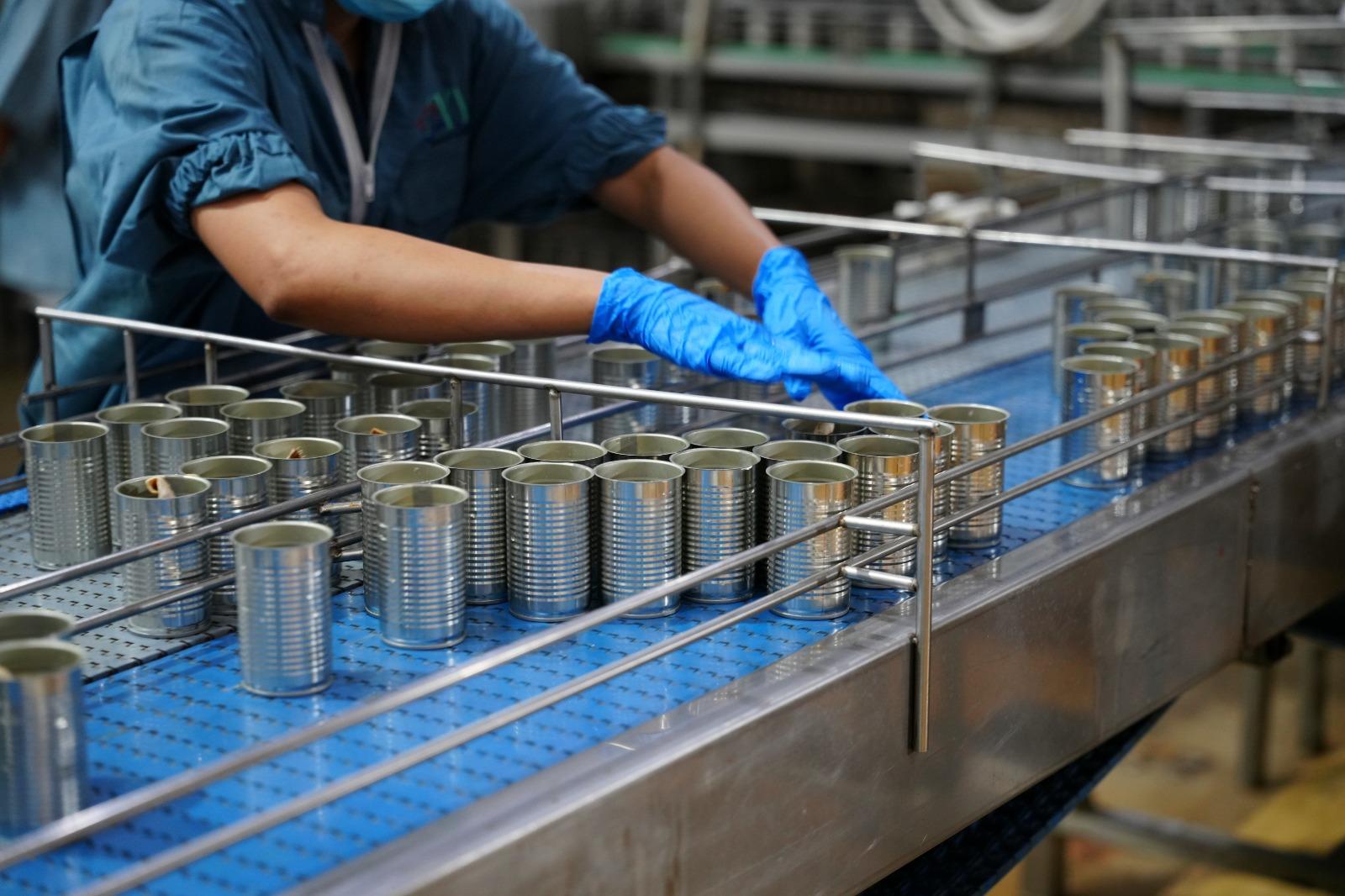 Dentro de uma fábrica, uma pessoa separa a fabricação de latas de alumínio.