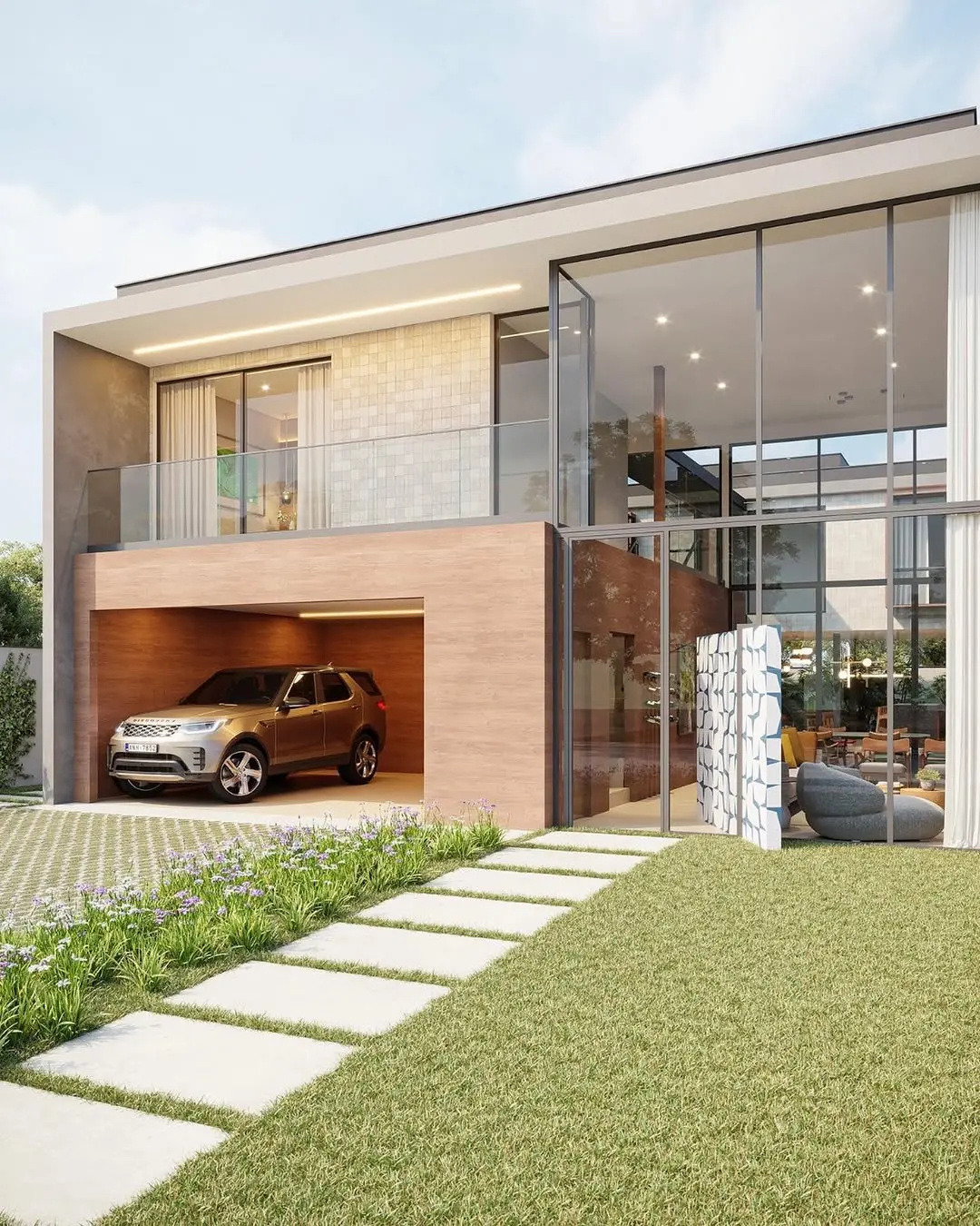 Na imagem, uma renderização arquitetônica de uma casa luxuosa e moderna de dois pavimentos durante o dia. A fachada apresenta linhas retas e grandes painéis de vidro que revelam um interior iluminado e decorado. No lado esquerdo, há uma garagem aberta revestida em madeira clara, onde está estacionado um SUV cor de bronze. Acima da garagem, uma varanda com guarda-corpo de vidro e parede em tons de bege. À direita, uma imponente fachada de vidro de pé-direito duplo destaca a área social. O jardim frontal possui um gramado verde impecável, um caminho de placas de concreto retangulares e um canteiro com pequenas flores arroxeadas. O céu está claro com nuvens leves, transmitindo uma atmosfera sofisticada e clean.