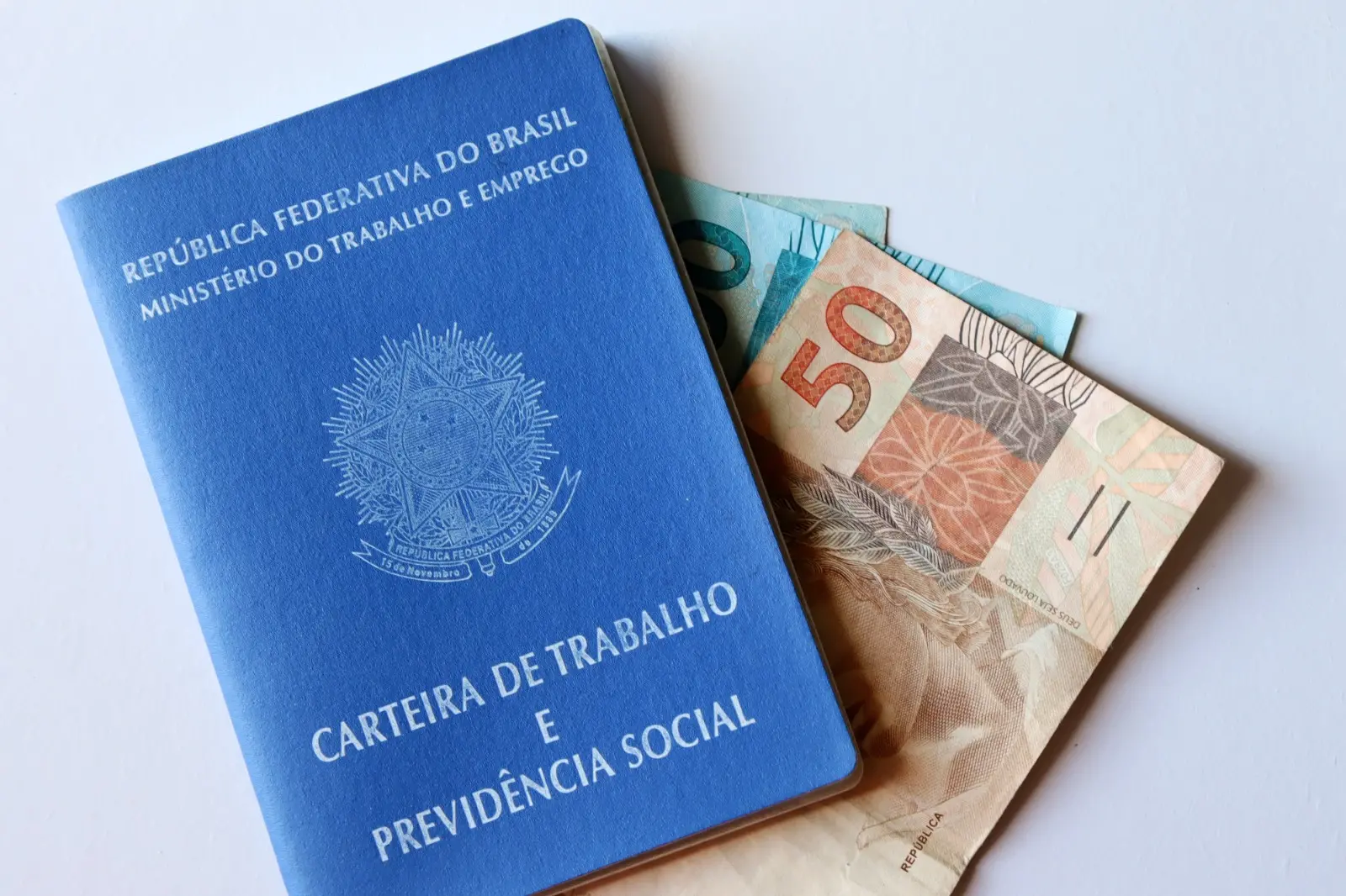 Uma carteira de trabalho em cima de uma mesa com umas cédulas em dinheiro dentro dela.