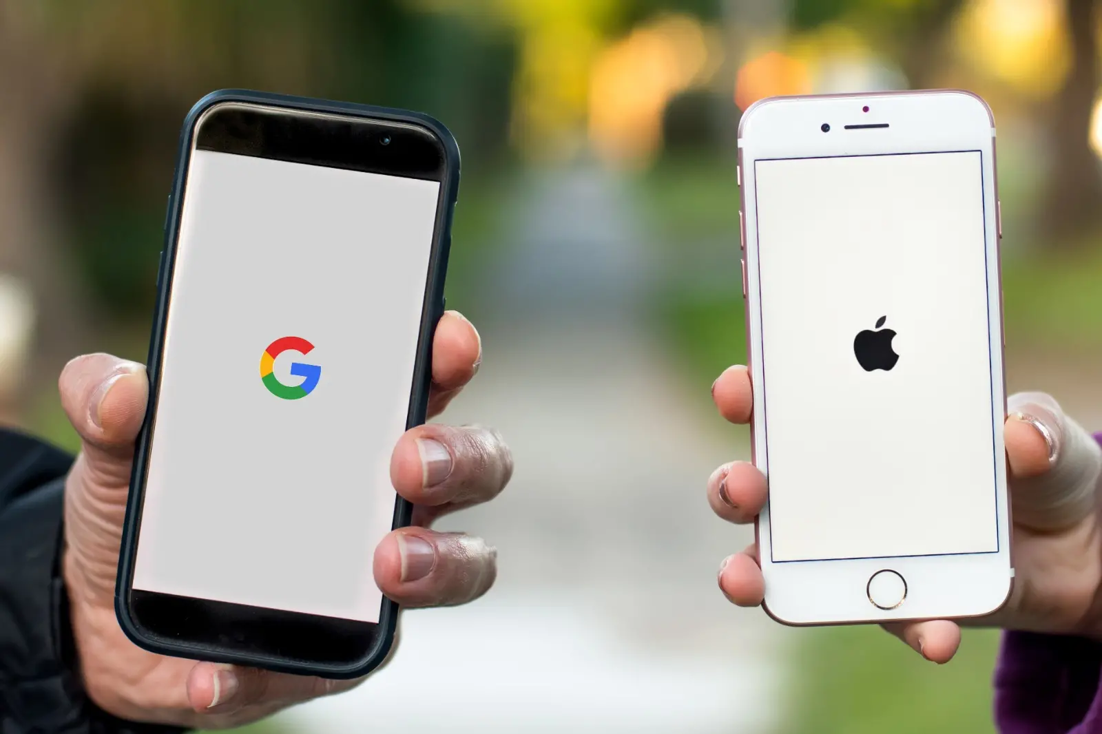 Duas pessoas seguram celulares em que mostram os símbolos do Google e da Apple.