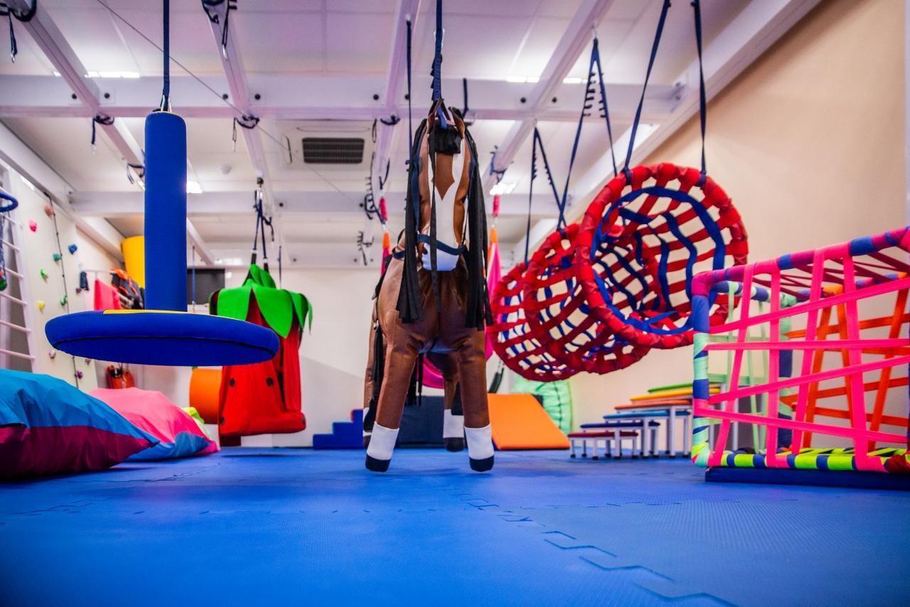 Ambiente terapêutico com balanços, estruturas suspensas e colchonetes coloridos.