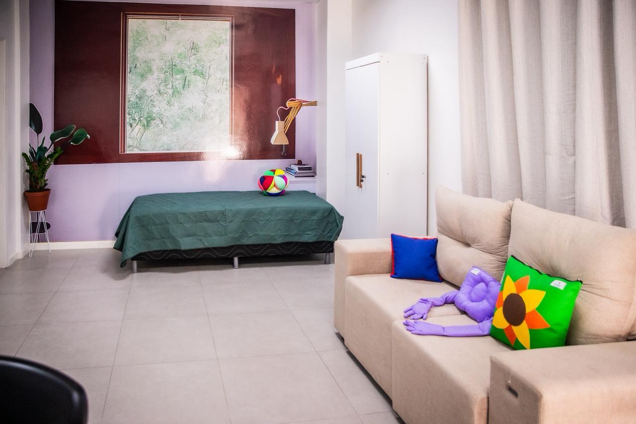 Sala com sofá, cama, guarda-roupas e almofadas, simulando um apartamento.