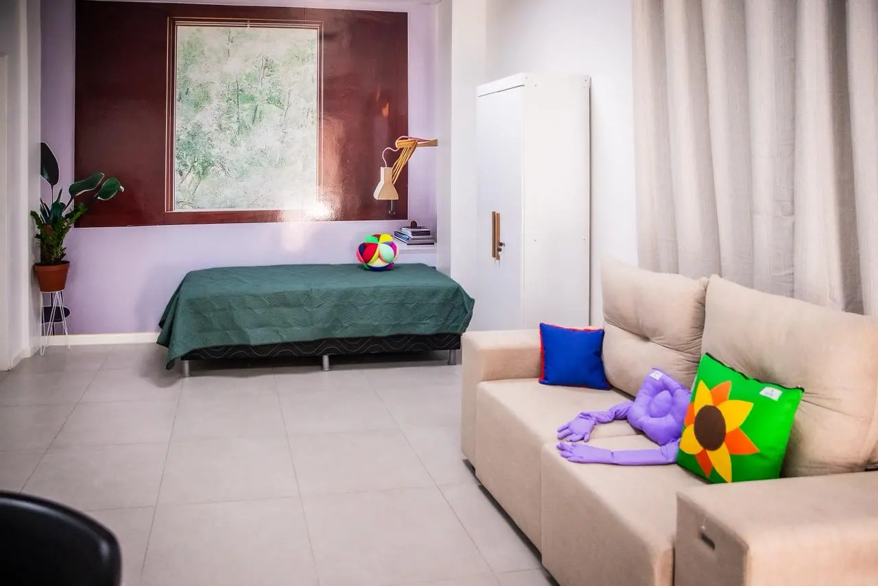 Sala com sofá, cama, guarda-roupas e almofadas, simulando um apartamento.