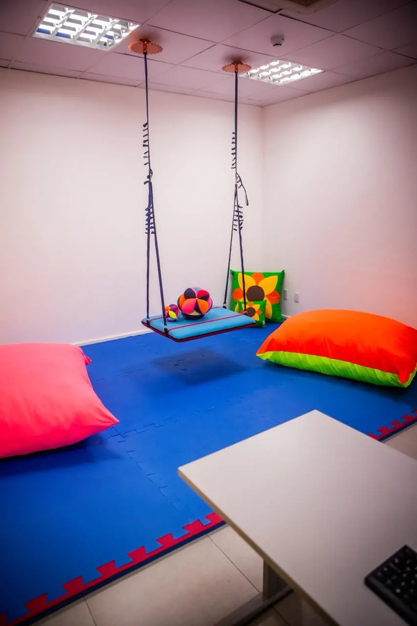 Sala com balanço terapêutico, almofadas grandes e piso emborrachado.