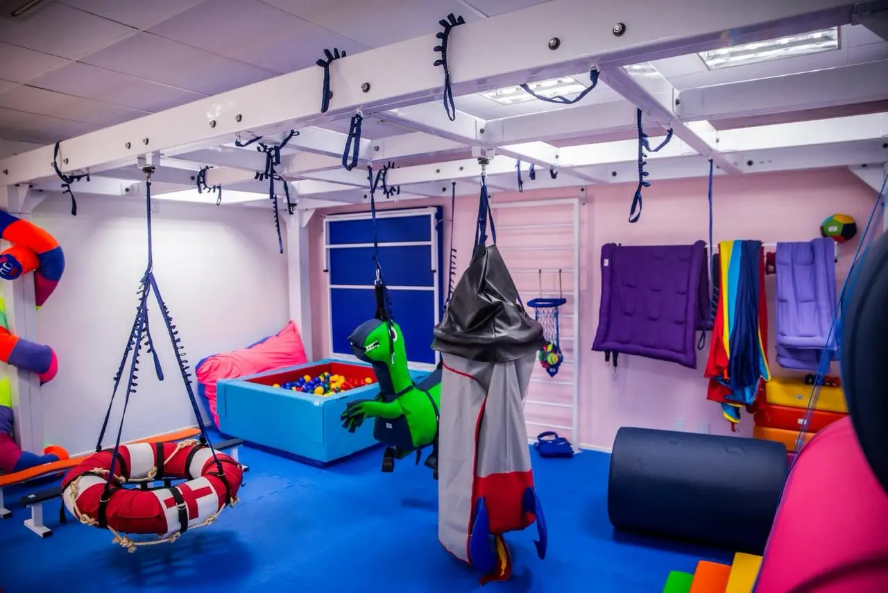 Sala de fisioterapia com brinquedos suspensos e piscina de bolinhas.