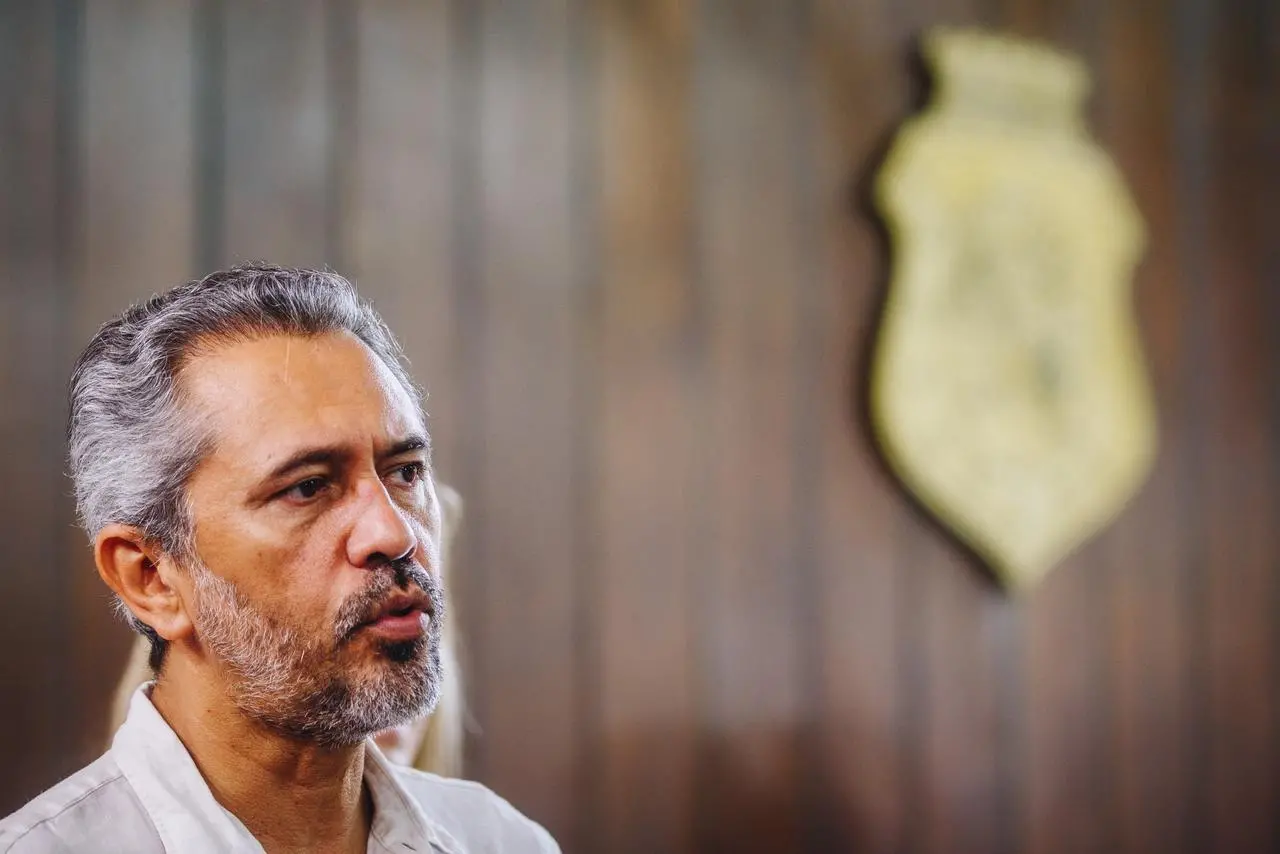 Elmano de Freitas durante entrevista. Ao fundo, o brasão do estado do Ceará.