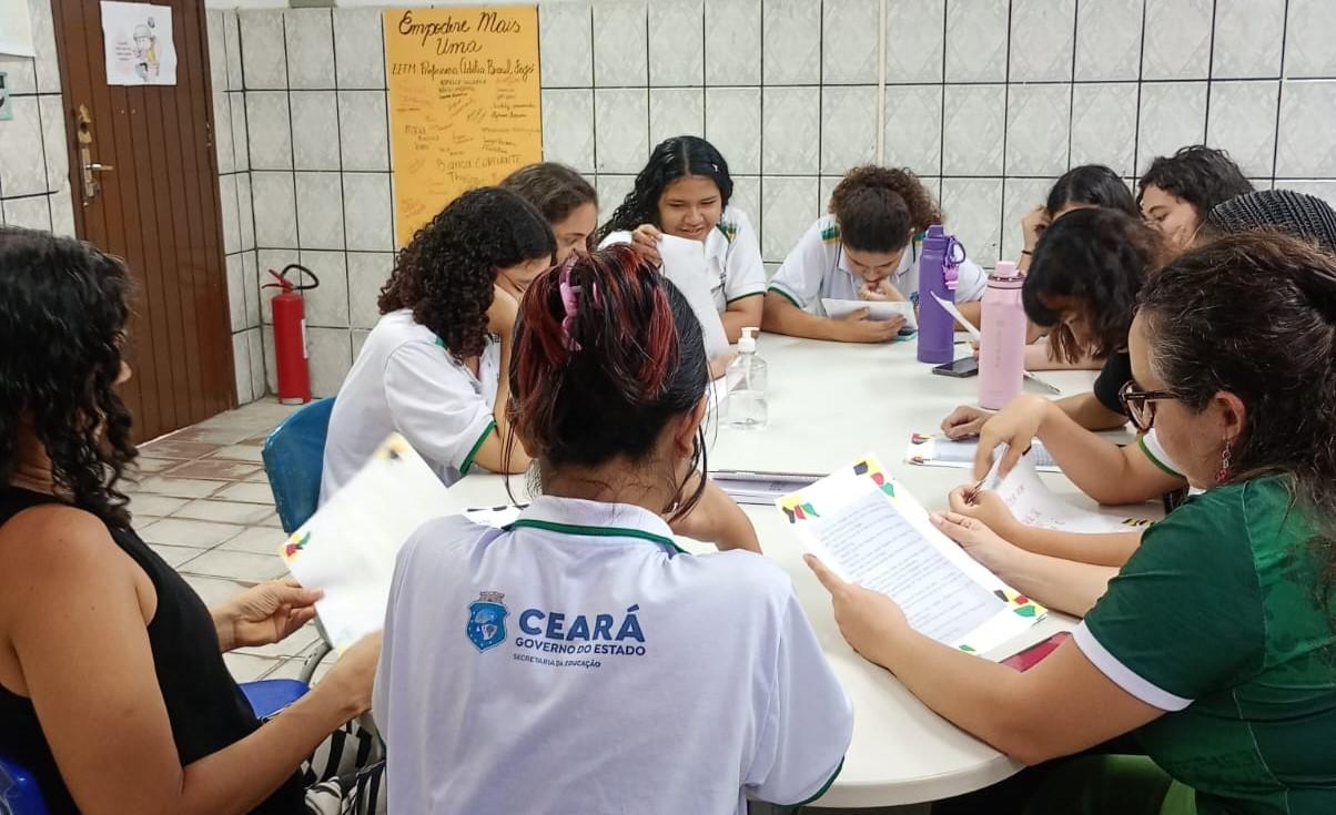 Grupo de profissionais de saúde e educadores reunidos em uma mesa, discutindo projetos sociais e trabalhando para empoderar mulheres e jovens na comunidade.