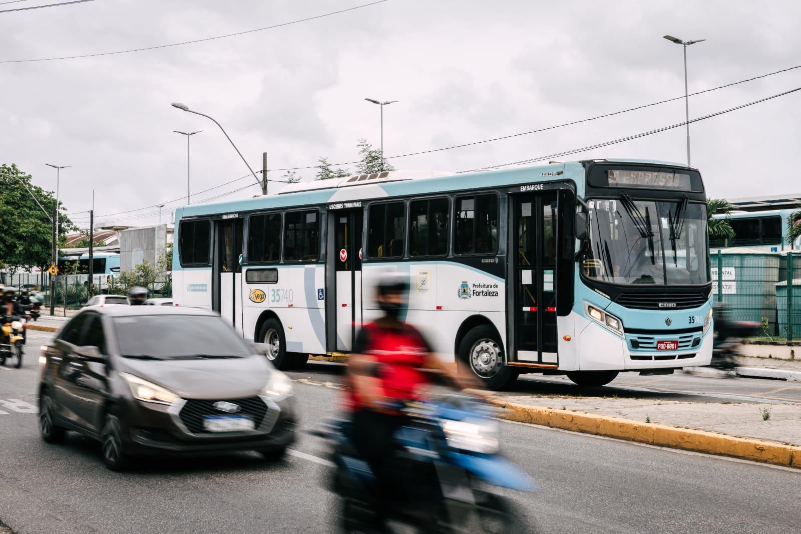 Foto de ônibus coletivo de Fortaleza, no Ceará, trafegando em via da cidade. O veículo é branco com detalhes em azul claro.