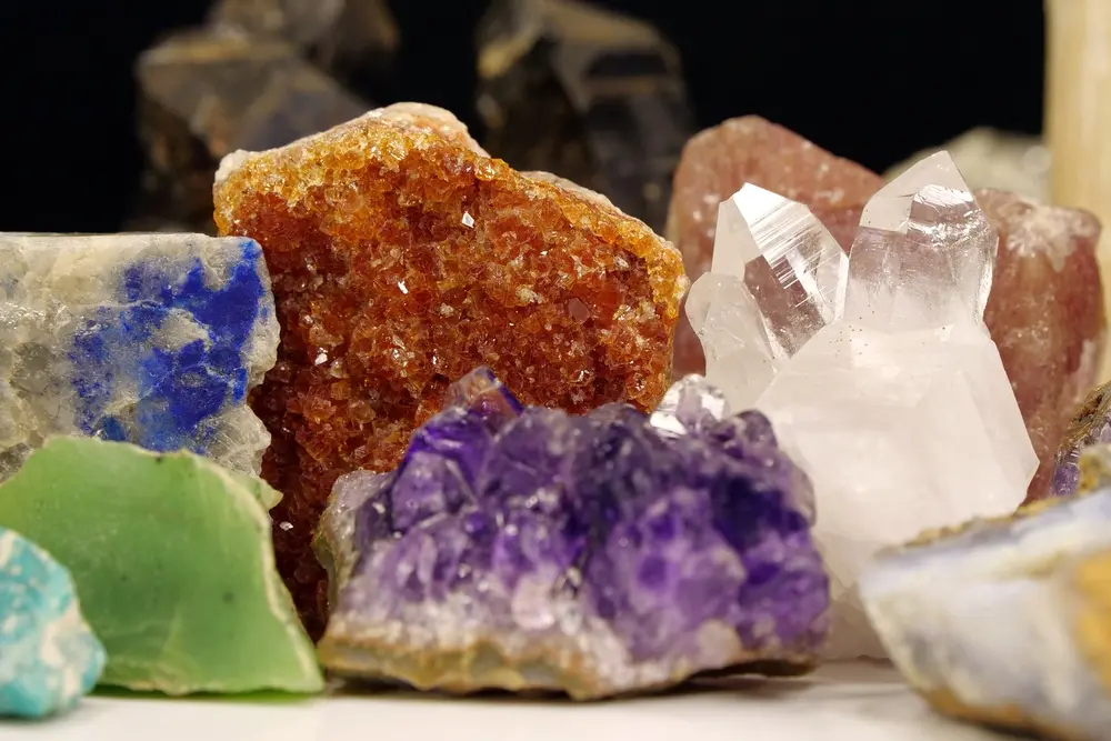 Coleção de diferentes cristais e minerais coloridos, incluindo ametista roxa, quartzo transparente, calcita verde, e outros minerais distintos em uma exposição