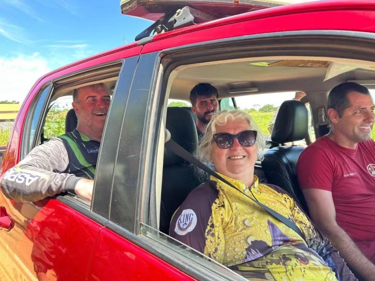 Família resgatada sendo encaminhada ao pronto-socorro dentro de carro vermelho acompanhados de um integrantes da equipe do corpo de bombeiros.