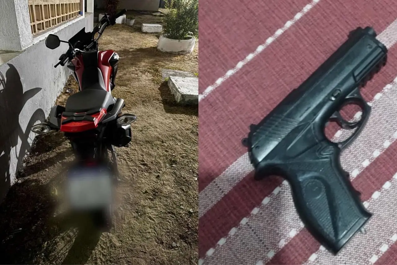 Imagem de uma motocicleta vermelha estacionada ao lado de uma parede e, ao lado, uma arma de fogo de pistola preta, colocada sobre uma superfície de tecido listrado. A foto pode indicar um contexto de segurança ou uso de armas.
